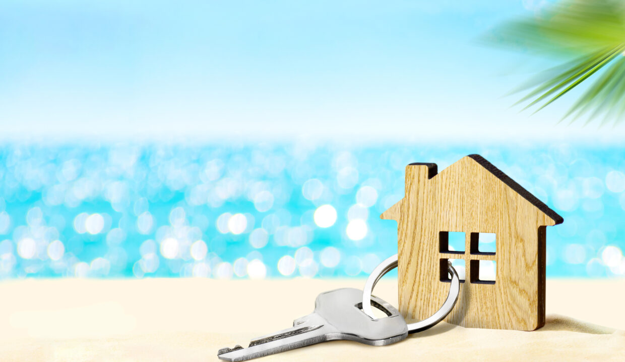 House by the sea concept. Figure of house and key on sandy beach